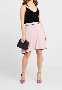 Musta laskostettu toppi, vaaleanpunaiset liehuvat hameet mustalla vyötäröllä, musta käsilaukku ja vaaleanpunaiset käärmeennahkakuosiset korkokengät.