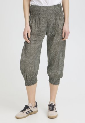 Person wearing loose, patterned cropped pants with elastic waist and cuffs, paired with white and black sneakers.