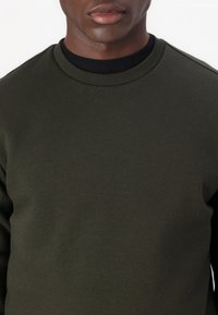 Mörkgrön sweatshirt med rundad halsringning, ribbad svart krage och strukturerad tyg. Enkel, åtsittande design utan synliga logotyper eller mönster.