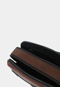 Borsa in pelle marrone con cerniere nere, dotata di tre scomparti e una texture liscia. Accentuata da cuciture lungo i bordi.