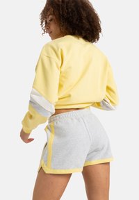 Sudadera amarilla corta con acentos a rayas grises y blancas, combinada con pantalones cortos grises con ribete amarillo a los lados. Tejido suave de mezcla de algodón.