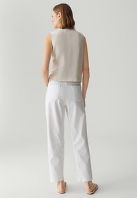 Mouwloze beige top gecombineerd met witte broeken. De top heeft een gladde textuur, terwijl de broeken van denim zijn gemaakt met achterzakken en een rechte snit.