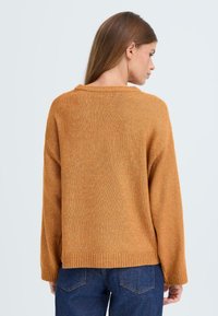 Maglione arancione oversize con lavorazione a coste, orlo a coste e maniche lunghe, abbinato a jeans in denim blu.