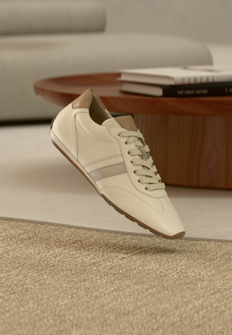 Baskets couleur crème en cuir texturé, accents marron clair et une bande gris clair. Elles comportent des lacets ronds et une semelle en caoutchouc.