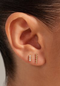 Boucles d'oreilles en or avec un design linéaire. Une boucle d'oreille présente trois pierres transparentes, tandis que l'autre affiche une série de petites perles rondes.