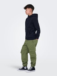 Felpa navy, pantaloni cargo oliva con tasche e sneakers alte nere. Design semplice con vestibilità rilassata e polsini a coste.