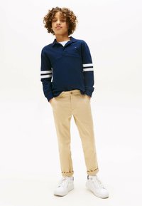 Marineblaues Langarmpolo mit weißen Streifen an den Ärmeln, kombiniert mit beigen Hosen und weißen Sneakers; lässige Passform, weicher Stoff und Kragen-Design.