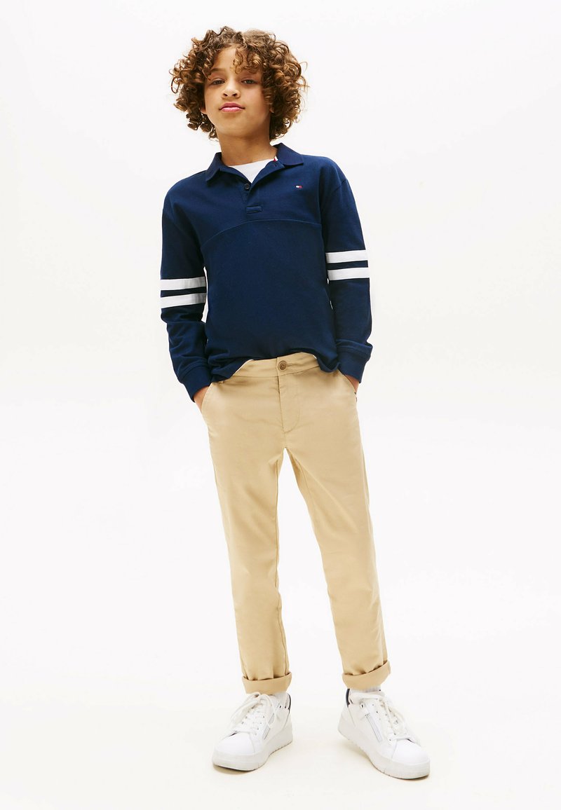 Marineblaues Langarmpolo mit weißen Streifen an den Ärmeln, kombiniert mit beigen Hosen und weißen Sneakers; lässige Passform, weicher Stoff und Kragen-Design.