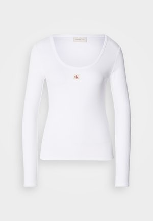 Camisola branca de manga longa feita de tecido canelado, com decote redondo e um pequeno logótipo retangular ao centro.