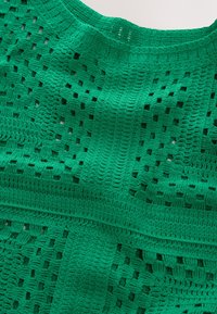 Roheline heegeldatud tekstiil, millel on avatud ja suletud mustrite segu, sile tekstuur ja struktureeritud kuju. Olemas dekoratiivsed ribadetailid.