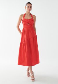 Punane kaeluseta kleit, millel on liibuv ülakeha ja lõikega detail, voolav astmeline seelik, valmistatud pehmest kangast. Kaasas valged rihmikandis sandaalid.