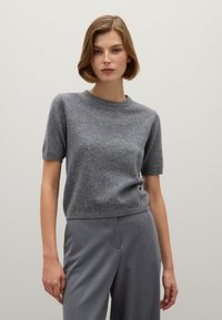Suéter gris de manga corta en punto suave y texturizado con escote redondo. Combinado con pantalones de traje grises, que muestran un ajuste casual.