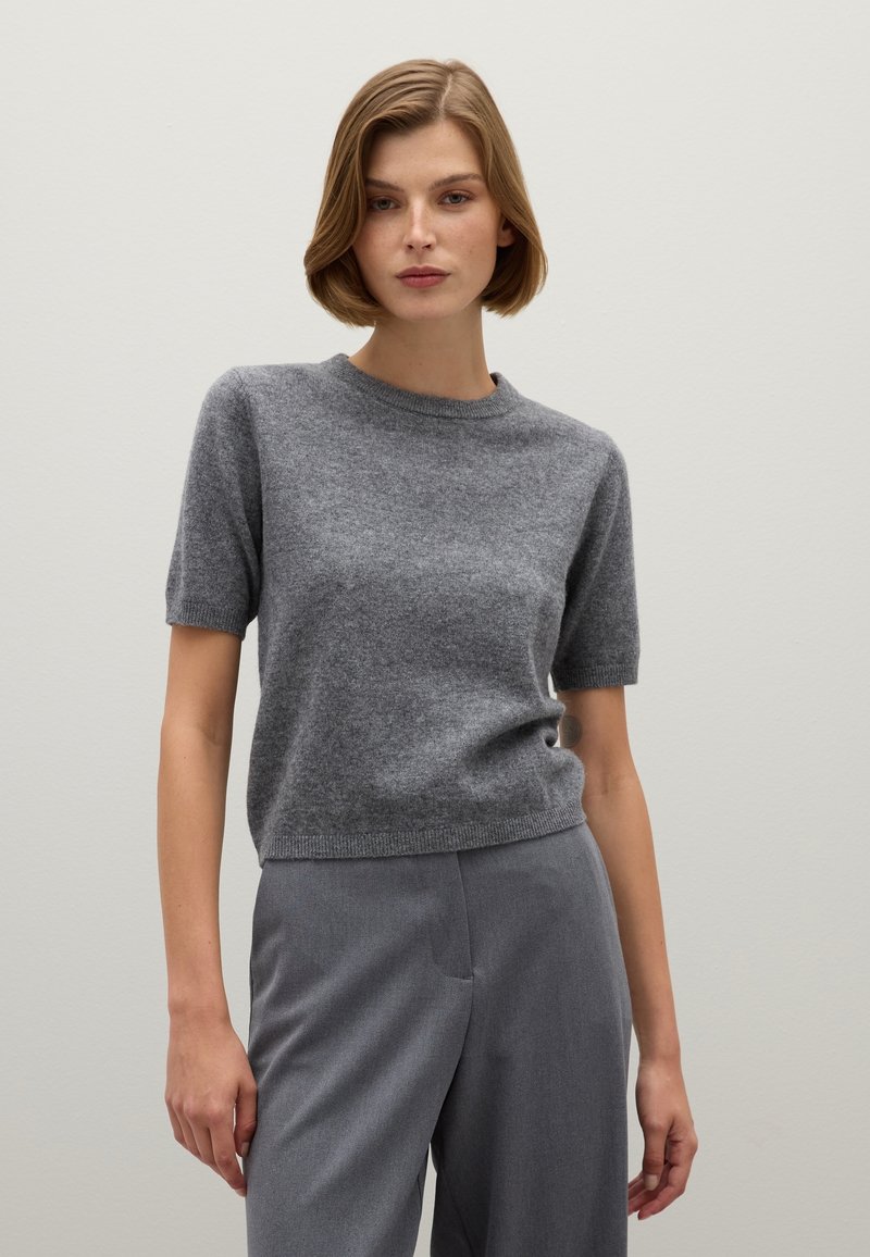 Suéter gris de manga corta en punto suave y texturizado con escote redondo. Combinado con pantalones de traje grises, que muestran un ajuste casual.