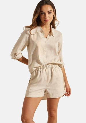 Chemise en lin beige avec un devant à boutons et des manches retroussées, associée à un short assorti doté d'une taille élastique et de poches latérales.