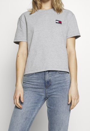 Graues, kurz geschnittenes T-Shirt aus Baumwolle mit kurzen Ärmeln; verfügt über ein kleines schwarz-rotes-weißes Logo auf der linken Brustseite.