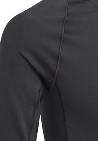 T-shirt de sport noir ajusté à manches longues avec une texture lisse, des coutures plates et un col haut. Le matériau semble extensible et durable.