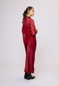 Bluza roșie din dantelă cu mâneci lungi, purtată peste o fustă roșie din satin. Cizme negre până la gleznă. Părul este stilizat cu o panglică neagră.