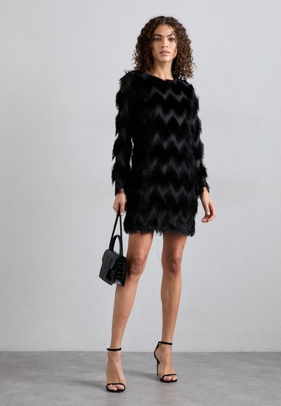 Μαύρο κοντό φόρεμα με ζιγκ-ζαγκ σχέδιο, φτιαγμένο από ψεύτικη γούνα. Διαθέτει μακριά μανίκια, κρόσσια και εφαρμοστή σιλουέτα. Συνδυασμένο με μαύρη τσάντα.