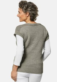 Grauer gestrickter Pullover mit kurzen Ärmeln, geripptem Saum, strukturiertem Stoff und lockerer Passform, kombiniert mit einem weißen Langarmshirt darunter.