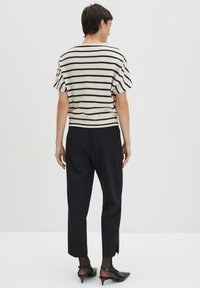 Top a maglia con strisce zigzag bianche e nere, maniche corte, abbinato a pantaloni neri con fessure laterali e scarpe con tacco nere.