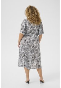 Robe maxi fleurie avec des manches courtes bouffantes, présentant un motif de feuilles noir et blanc sur un tissu léger, taille cintrée et jupe fluide.