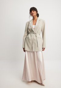 Light grey tailored blazer with a belted waist, featuring a single breast pocket, paired with a flowing pale pink satin maxi skirt.