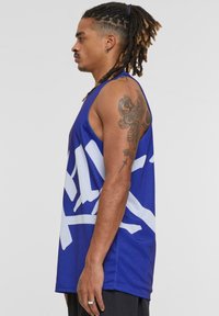 Canottiera sportiva blu in rete con grafiche astratte bianche, design senza maniche e vestibilità ampia, evidenziata da un collo rotondo.