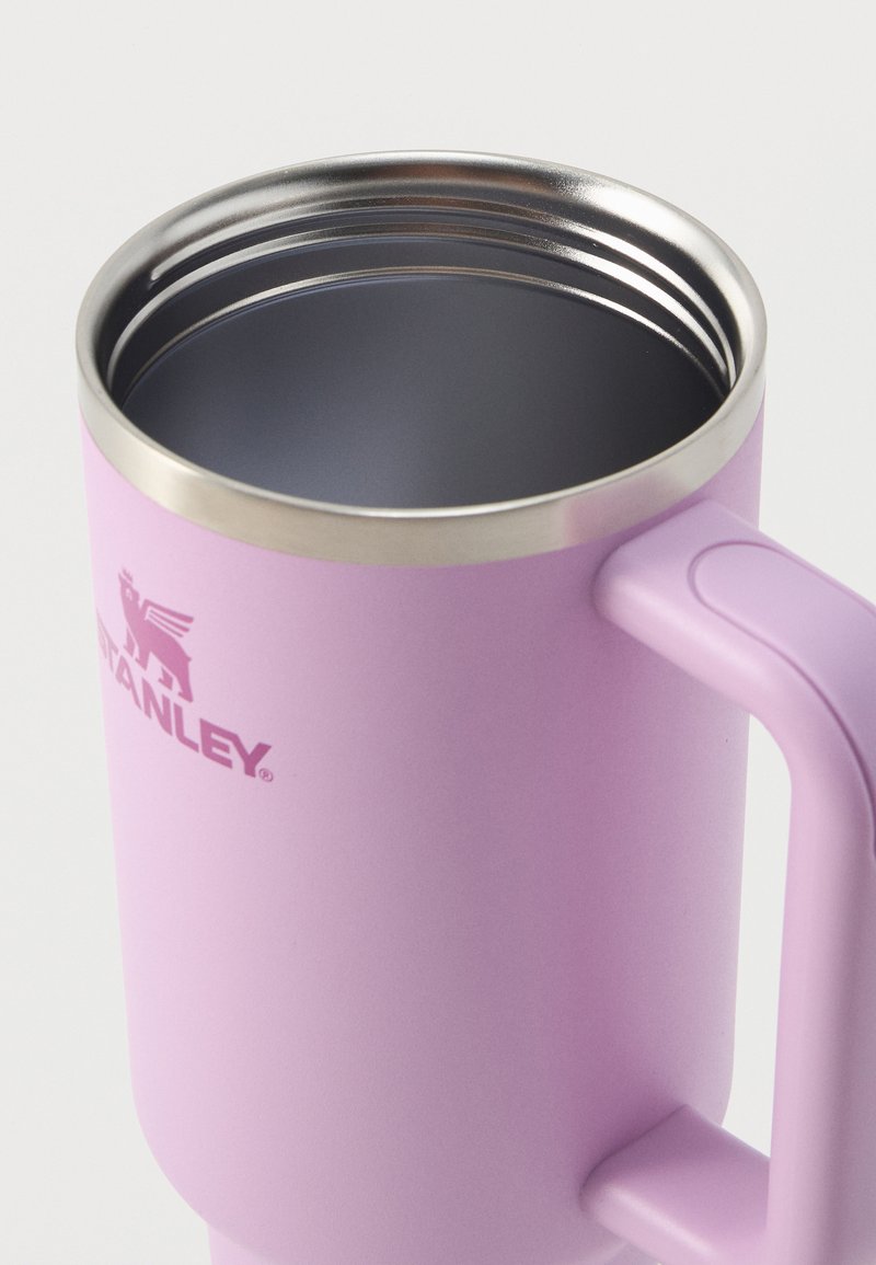 Taza aislante de acero inoxidable rosa con asa y parte superior abierta que muestra la superficie interior de color gris oscuro y parte del logo "Stanley".