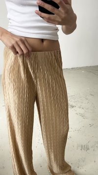 Pantaloni in tessuto dorato chiaro con un motivo a pieghe e texture. Vestibilità ampia con una vita elastica, caratterizzati da sottili linee verticali su tutta la superficie.