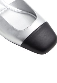 Zapatos planos de cuero metálico plateado con puntera de cuero negro. Presentan un diseño recortado y una textura lisa. Construcción ligera.