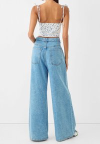 Light blue wide-leg jeans made of denim with two back pockets. Paired with a white floral crop top featuring tie straps.