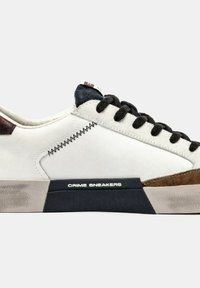 Baskets blanches avec des accents en suède marron et noir, ornées de détails cousus, de lacets noirs et d'une semelle en caoutchouc. Nom de la marque affiché sur le côté.