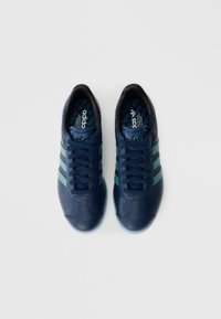 Marineblauwe sportschoenen met een gestructureerde bovenkant, drie teal strepen en donkerblauwe veters. Voorzien van een logo op de tong en een patroon op de binnenzool.