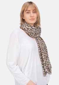 Écharpe imprimée léopard en tons beige et marron, en tissu léger, texture douce, élégamment drapée autour du cou, associée à un haut blanc.