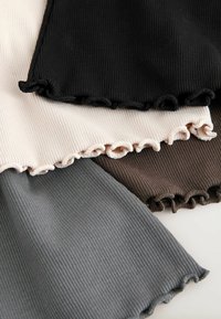 Quatre morceaux de tissu côtelé en noir, beige, marron et gris avec des ourlets à bord ondulé disposés en chevauchement sur une surface blanche.