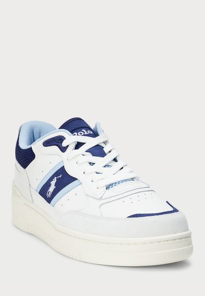 White sneakers with blue accents, featuring a synthetic upper, perforated toe box, and prominent branding. Thick rubber sole with textured detailing.