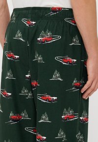 Zöld pizsama nadrág, piros autók hóban való közlekedését ábrázoló mintával, zöld fákkal kiegészítve. Gumis derék és puha szövet anyag.