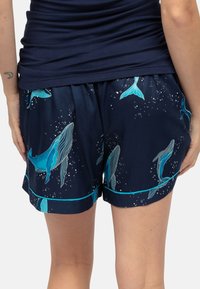 Granatowe szorty z wzorem niebieskich wielorybów i bąbelków, wykonane z miękkiej tkaniny z kontrastowym turkusowym obszyciem na dole.