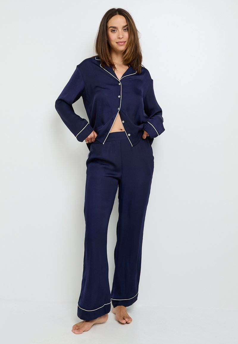 Ensemble de pyjama en satin bleu marine comprenant une chemise à bouton avec col, manches longues et passepoil blanc ; pantalons à jambe large avec une garniture similaire.