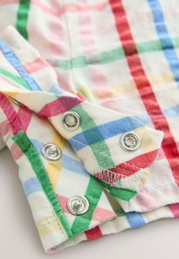 Checkered cotton fabric in red, green, blue, and yellow. Features silver snap fasteners and frayed edges on cuffs or collar.