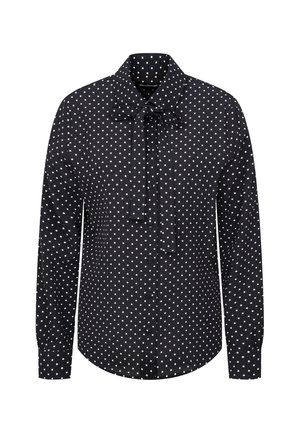 Zwarte blouse met lange mouwen, witte stippen, een knoopsluiting aan de voorkant en een strik bij de kraag.