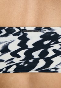 Calvin Klein midje med et svart og hvitt bølgete mønster, glatt tekstur og en liten, gravert logo-detalj.