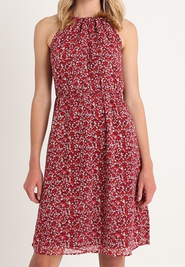 Robe rouge sans manches à col licou avec un motif floral rose et blanc, encolure froncée, taille cintrée, longueur genou sur une personne à la peau claire.