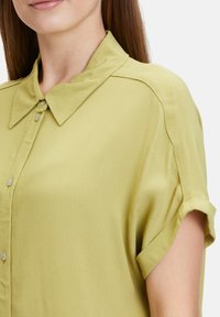 Short-sleeve, button-up shirt in light green fabric with a smooth texture. Features a pointed collar and rolled cuffs for a casual look.
