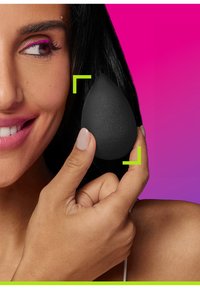 Una spugna per il trucco nera tenuta tra le dita, a forma di goccia d'acqua con una superficie liscia. Sfondo di un colore rosa brillante e verde.