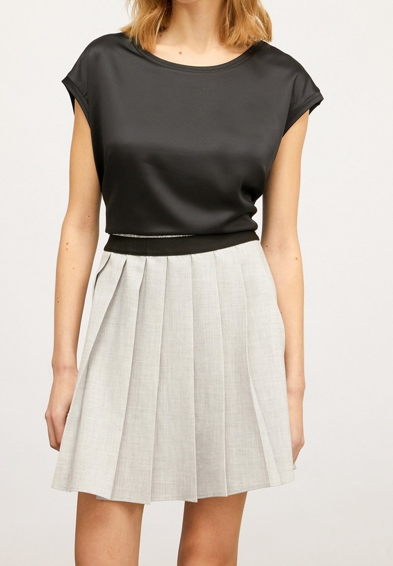 Haut en satin noir avec des manches courtes roulées et un col rond. Jupe plissée grise avec une taille ajustée noire et une texture légère.