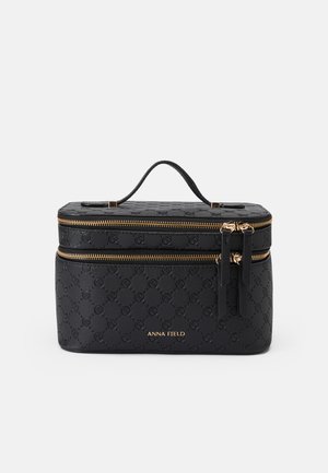 Trousse de toilette noire texturée avec des zips dorés, design à double compartiment, poignée supérieure et logo embossé sur le devant.