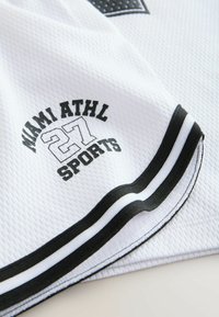 Tissu sportif blanc avec texte noir "MIAMI ATHL 27 SPORTS" et bordure à rayures noires et blanches sur le bord du matériau.