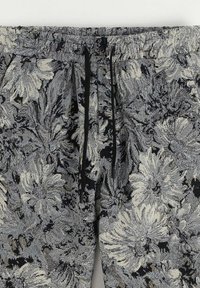 Pantalons à motif floral en noir, blanc et gris. Dotés d'une taille élastique et d'un cordon de serrage. Fabriqué en tissu texturé avec des détails complexes.