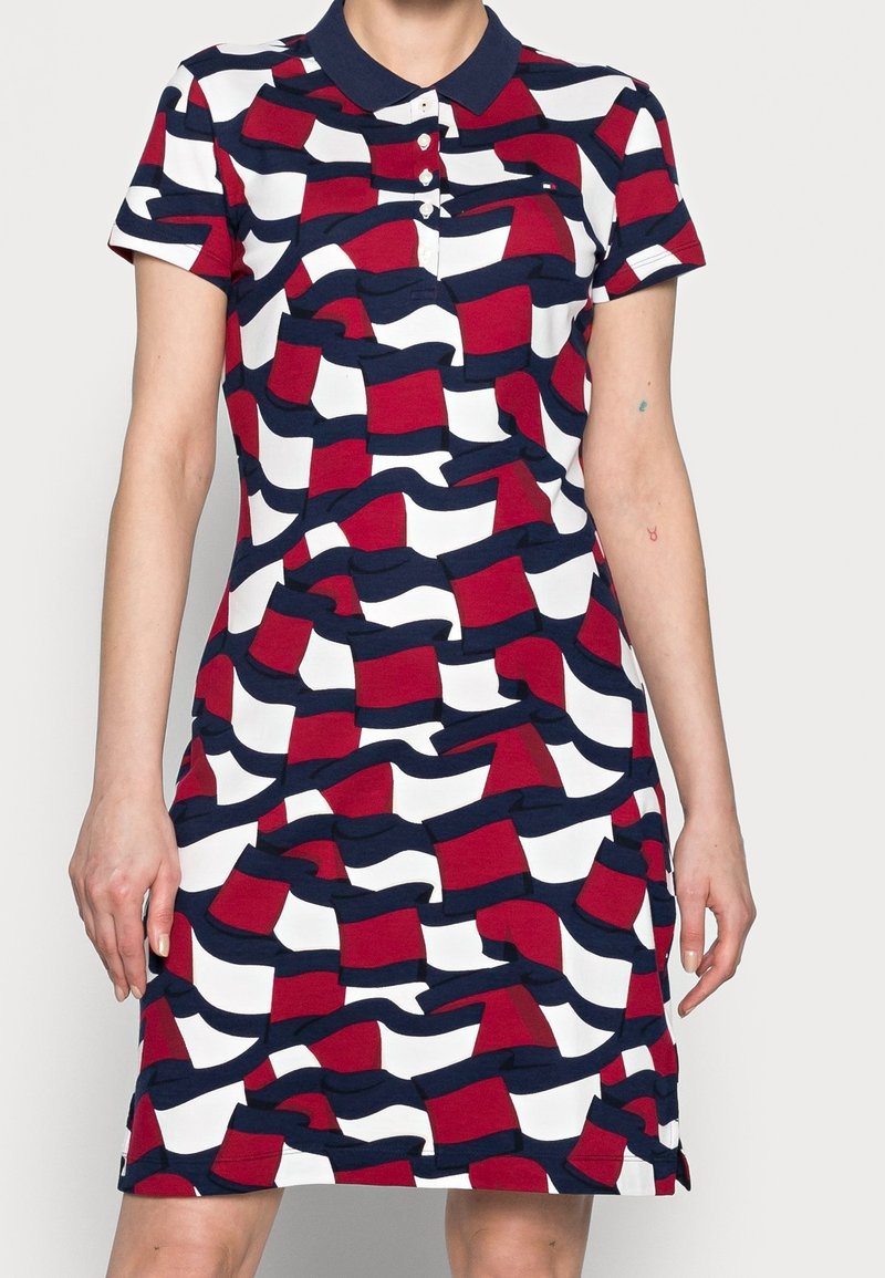 Femme portant une robe courte à manches courtes jusqu'aux genoux avec un col bleu marine et un motif abstrait de drapeau rouge, blanc et bleu marine.